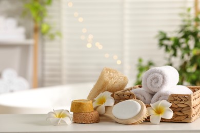 Photo of Composition with different spa products and plumeria flowers on white table in bathroom. Space for text