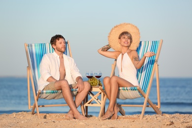 Young couple having picnic with wine and grapes on beach