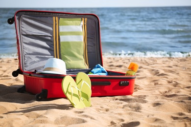 Open suitcase with stylish beach accessories on sand near sea. Space for text