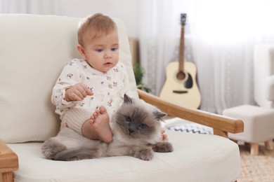 Photo of Cute little baby with adorable cat on armchair at home