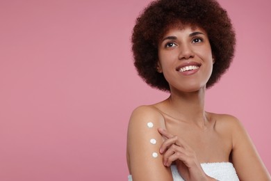 Beautiful young woman applying body cream onto arm on pink background, space for text