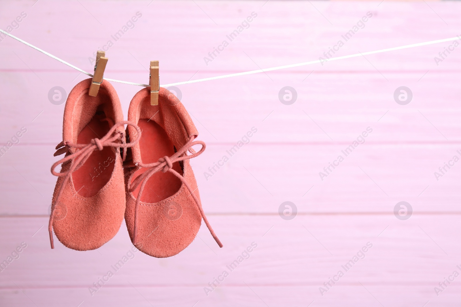 Photo of Pair of shoes on laundry line against pink wooden background, space for text. Baby accessories