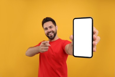 Photo of Young man showing smartphone in hand and pointing at it on yellow background, selective focus. Mockup for design