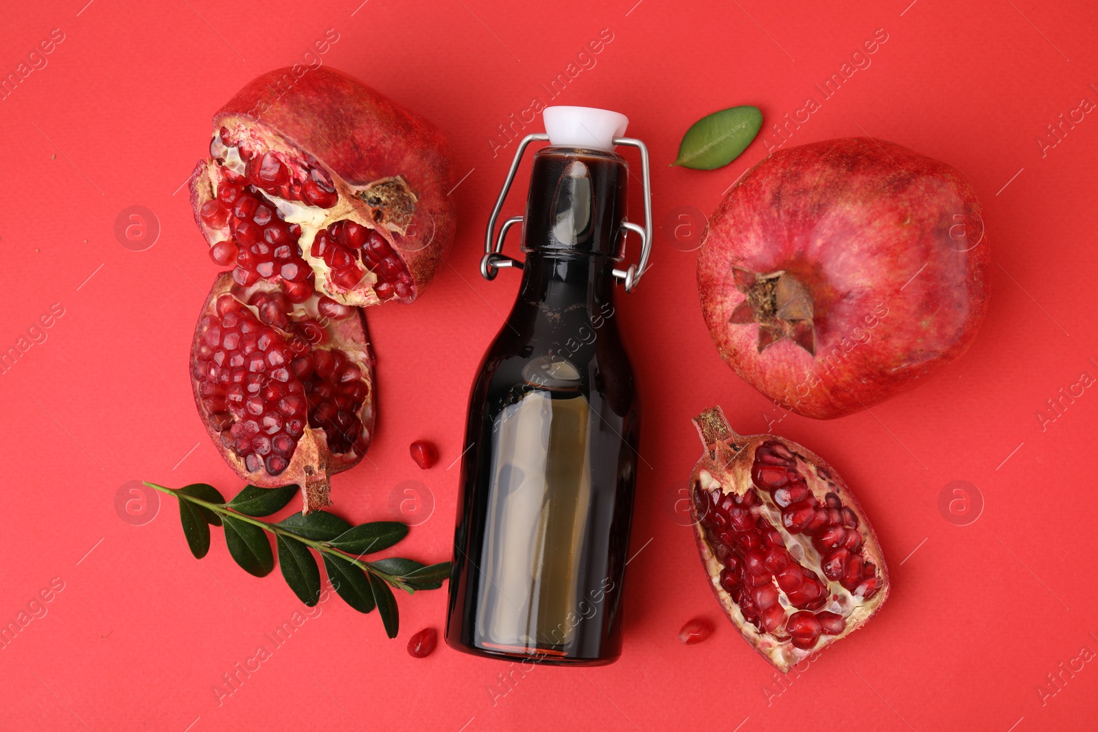 Photo of Tasty pomegranate sauce in bottle and fruits on red background, flat lay