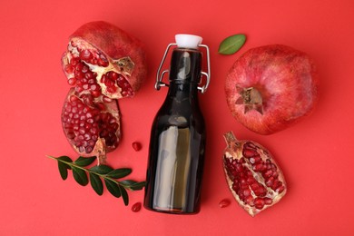 Photo of Tasty pomegranate sauce in bottle and fruits on red background, flat lay