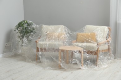 Photo of Stylish chairs, table and houseplant covered with plastic film at home