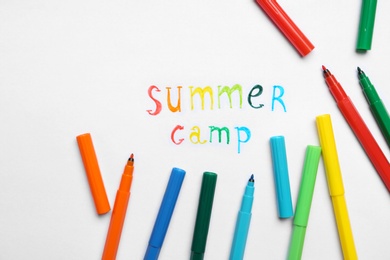 Photo of Text SUMMER CAMP and colorful felt tip pens on white paper, flat lay