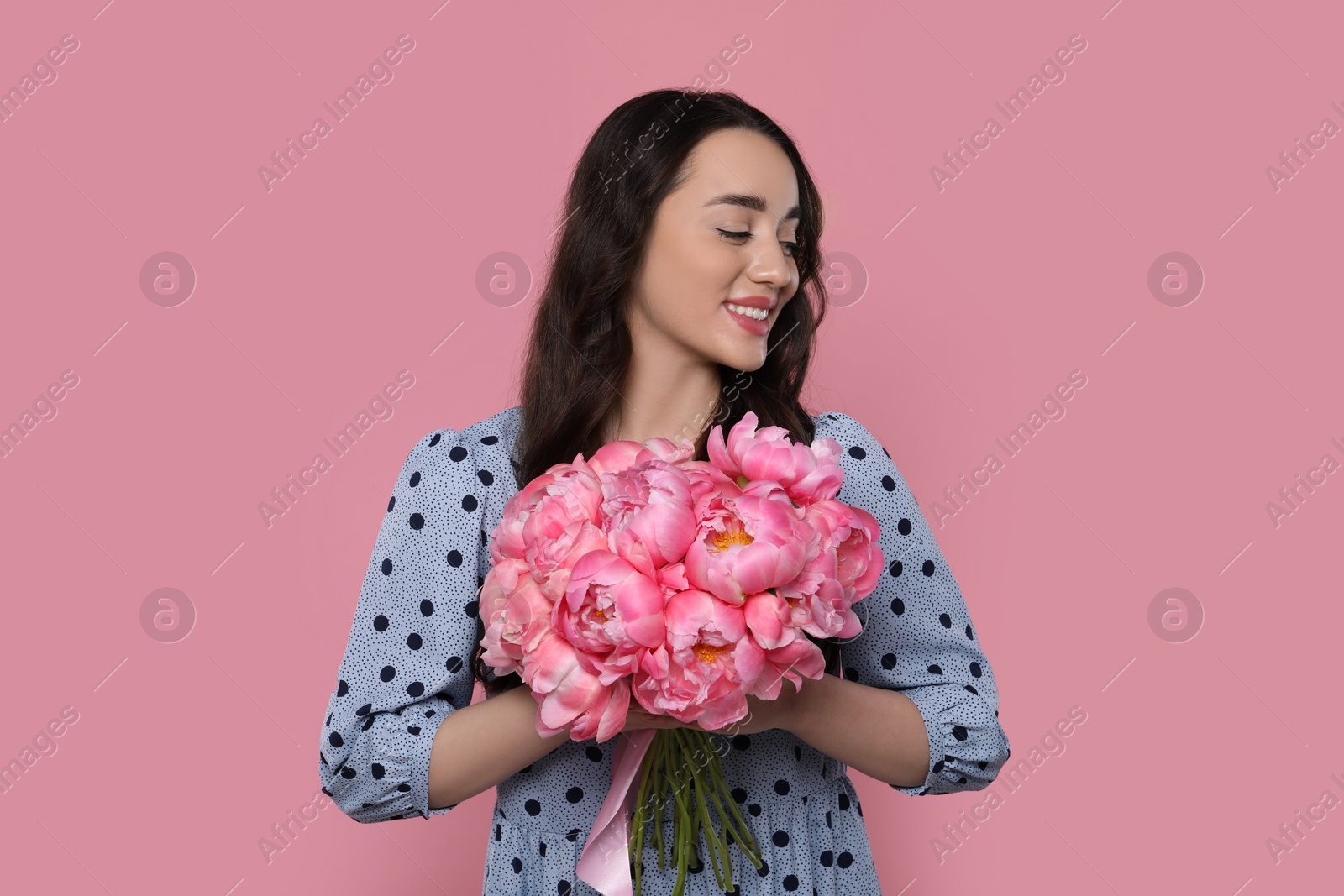 Photo of Beautiful young woman with bouquet of peonies on pink background