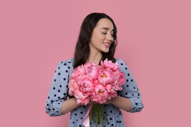 Beautiful young woman with bouquet of peonies on pink background