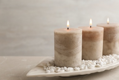 Photo of White plate with three burning candles and rocks on table. Space for text