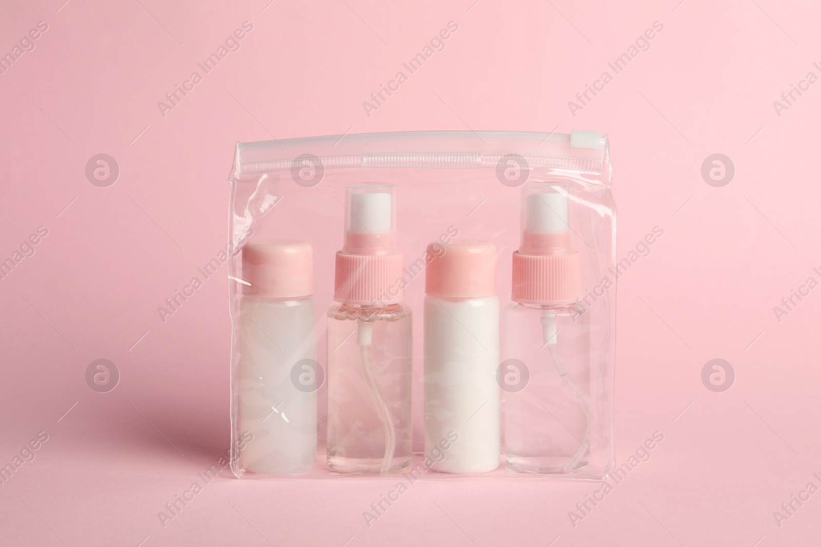 Photo of Cosmetic travel kit in plastic bag on pink background