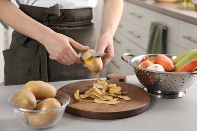 Photo of Woman peeling fresh potato with knife at light table indoors, closeup