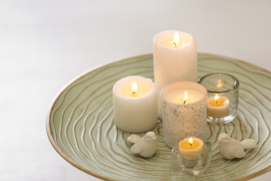 Photo of Beautiful burning candles on tray against light background