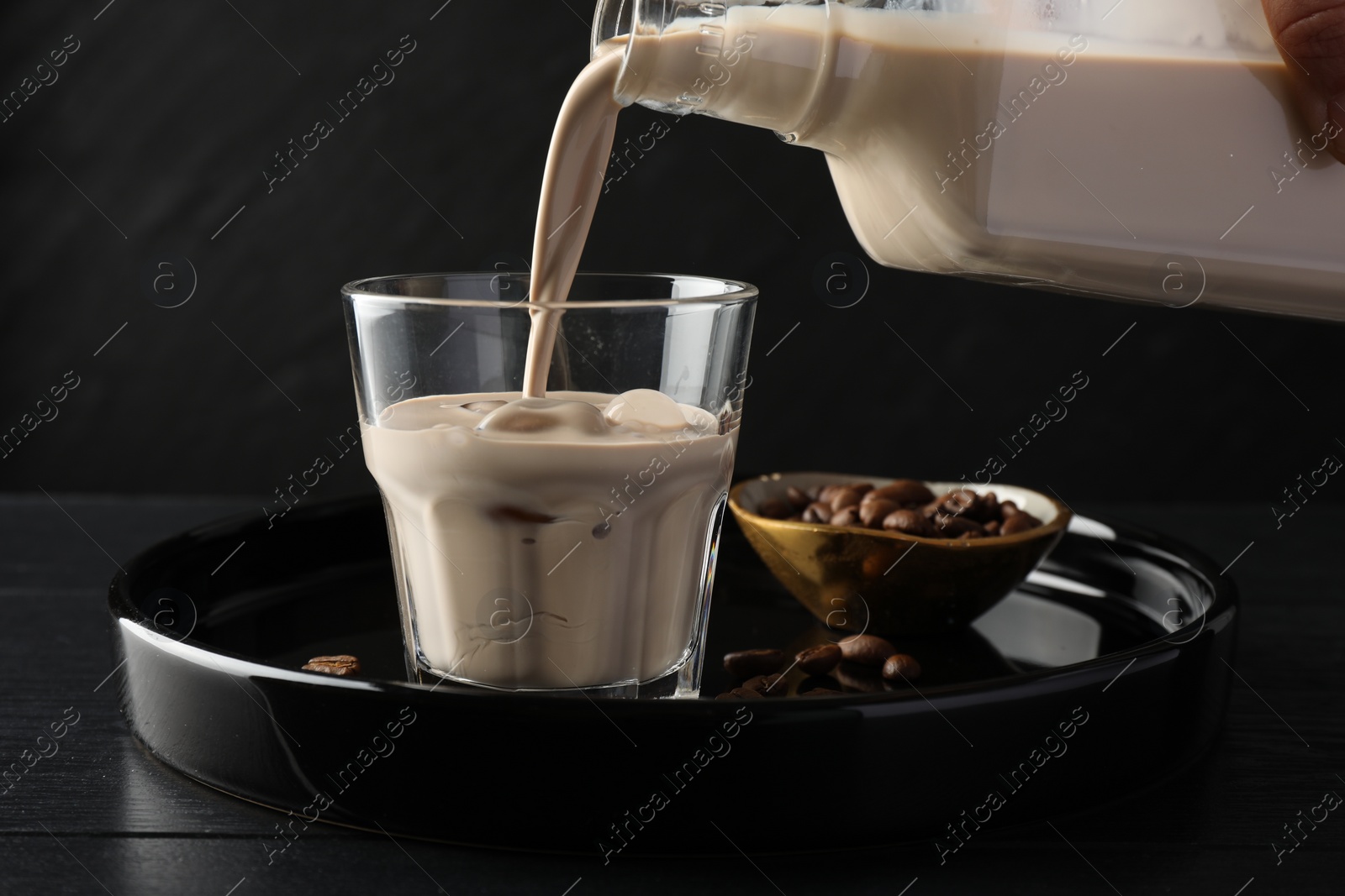 Photo of Pouring coffee cream liqueur into glass at black wooden table, closeup