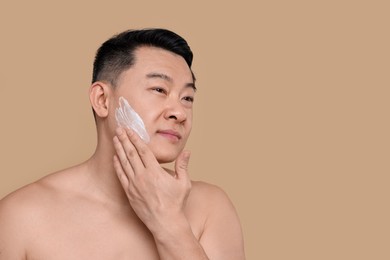 Photo of Handsome man applying cream onto his face on light brown background. Space for text