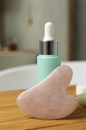 Photo of Rose quartz gua sha tool and cosmetic product on wooden bath caddy, closeup