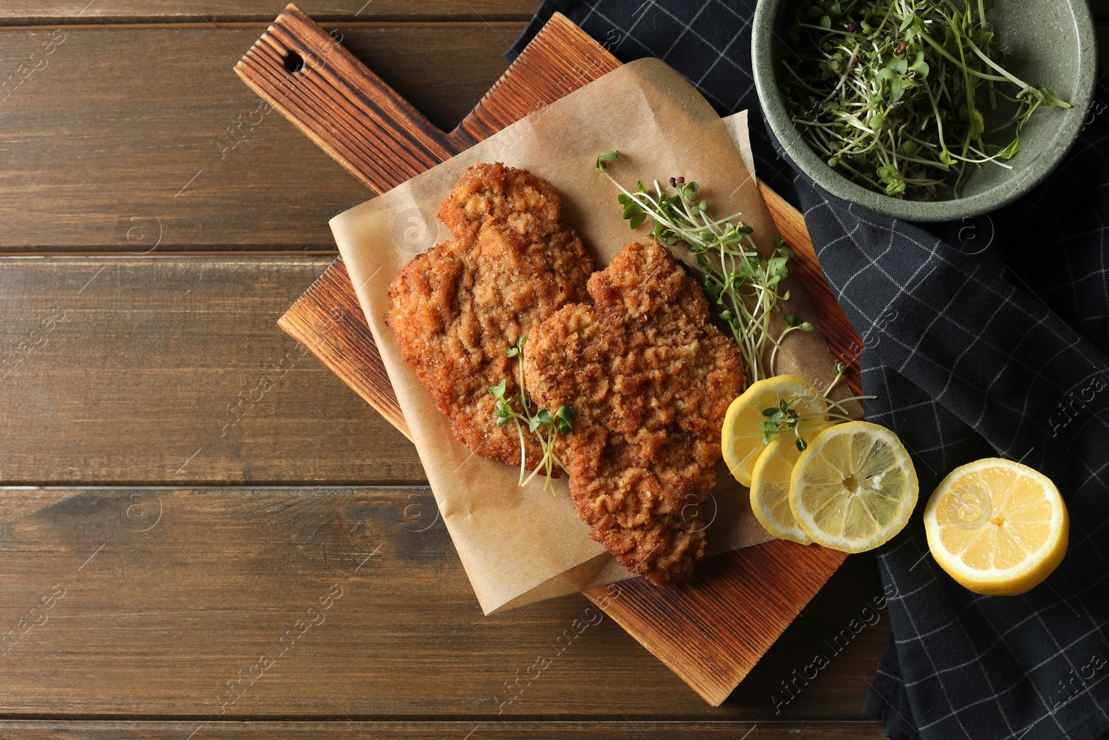 Photo of Tasty schnitzels served with lemon and microgreens on wooden table, flat lay. Space for text