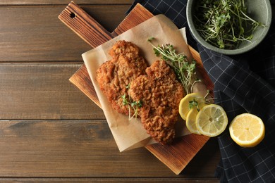 Tasty schnitzels served with lemon and microgreens on wooden table, flat lay. Space for text