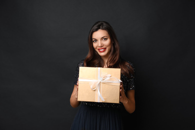 Beautiful woman with Christmas gift on black background