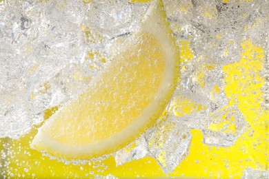 Photo of Juicy lemon slice and ice cubes in soda water against yellow background, closeup