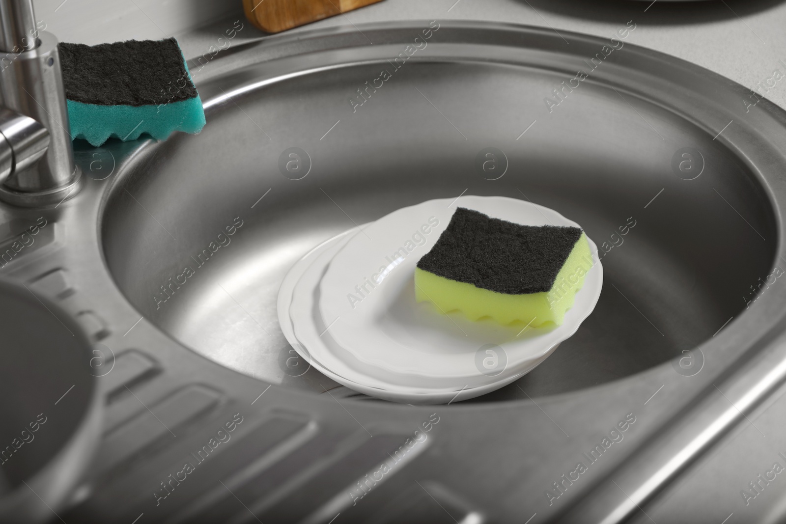 Photo of White plates and sponges in kitchen sink. Washing dishes