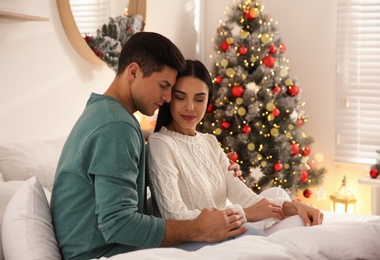 Happy couple on bed near Christmas tree at home