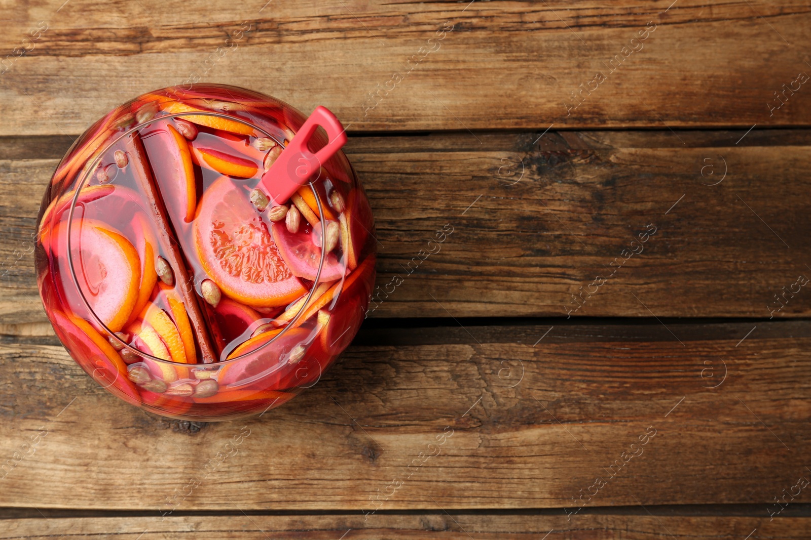 Photo of Glass bowl of aromatic punch drink on wooden table, top view. Space for text