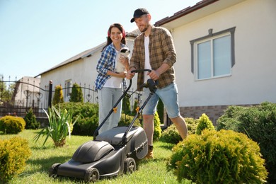Photo of Happy couple spending time together while cutting green grass with lawn mower in garden