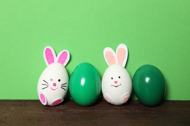 Photo of Two eggs as cute bunnies among others on wooden table against green background. Easter celebration