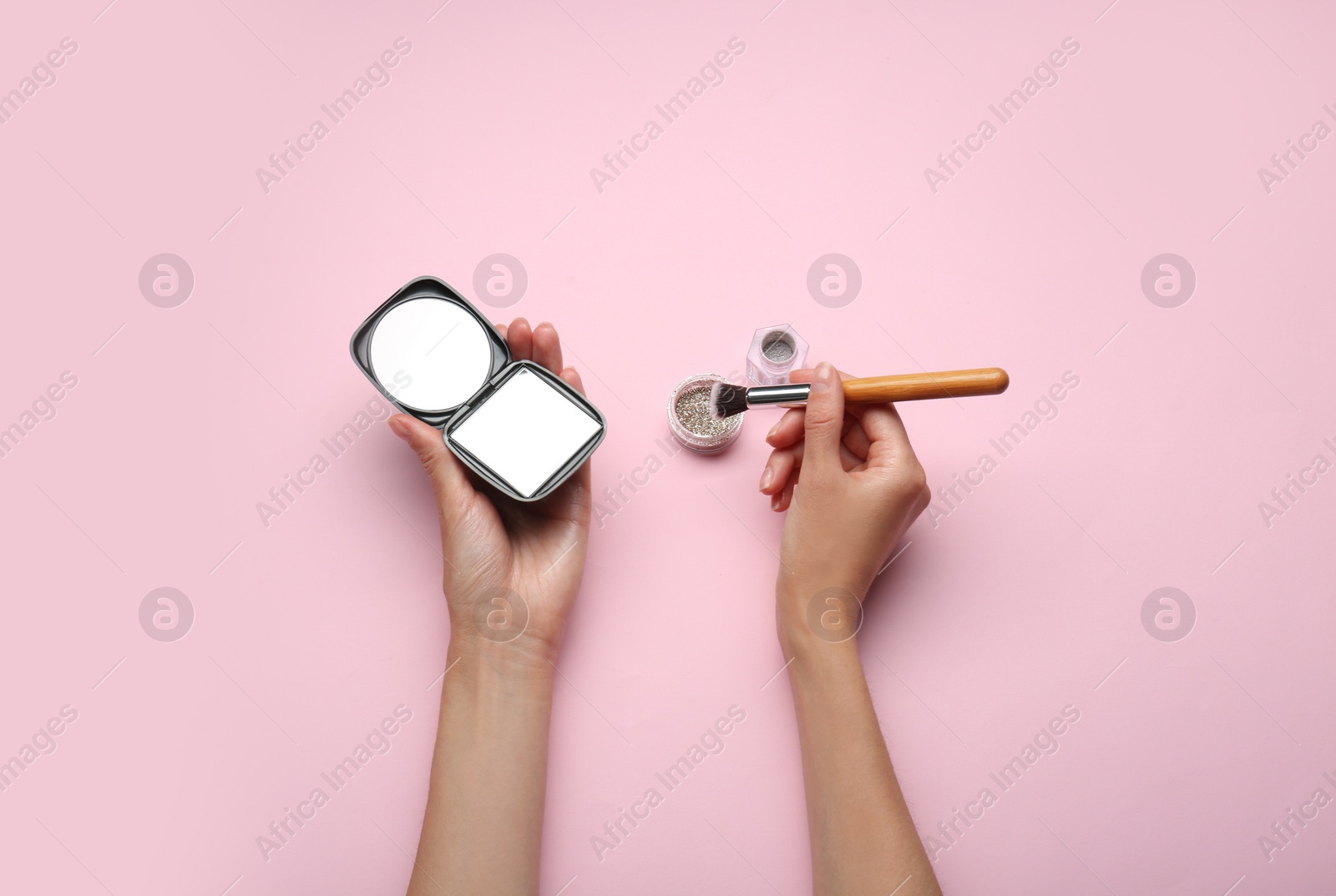 Photo of Woman holding pocket mirror and brush on pink background, top view