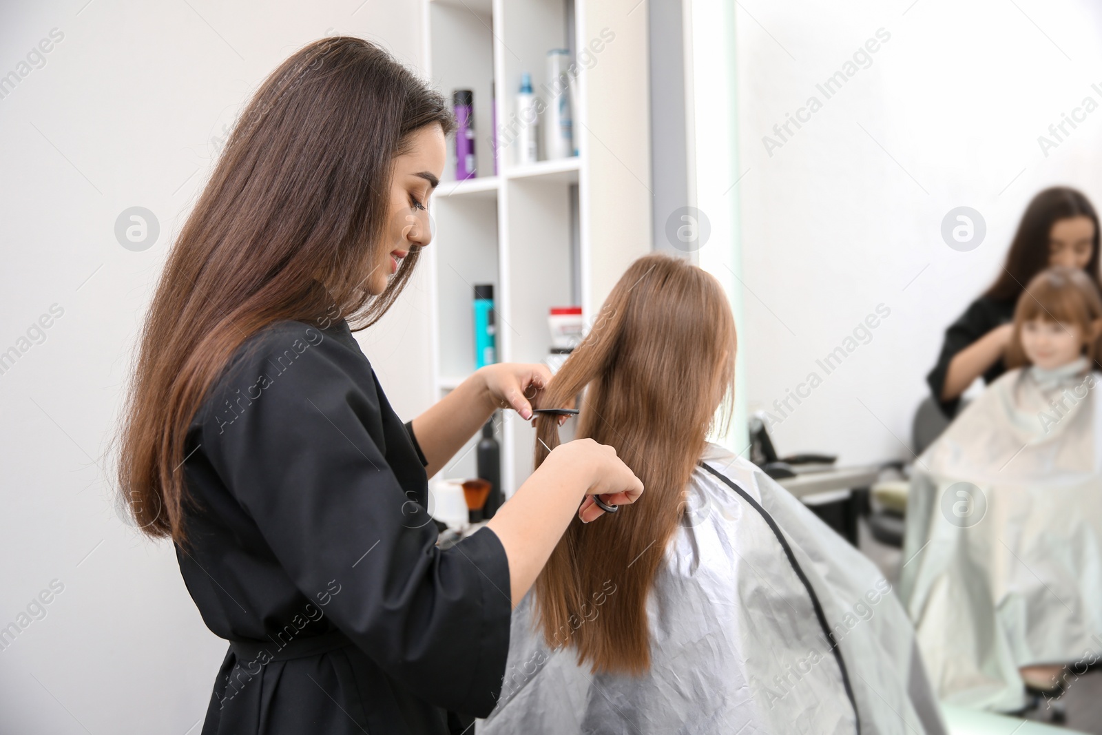 Photo of Professional female hairdresser working with little girl in salon