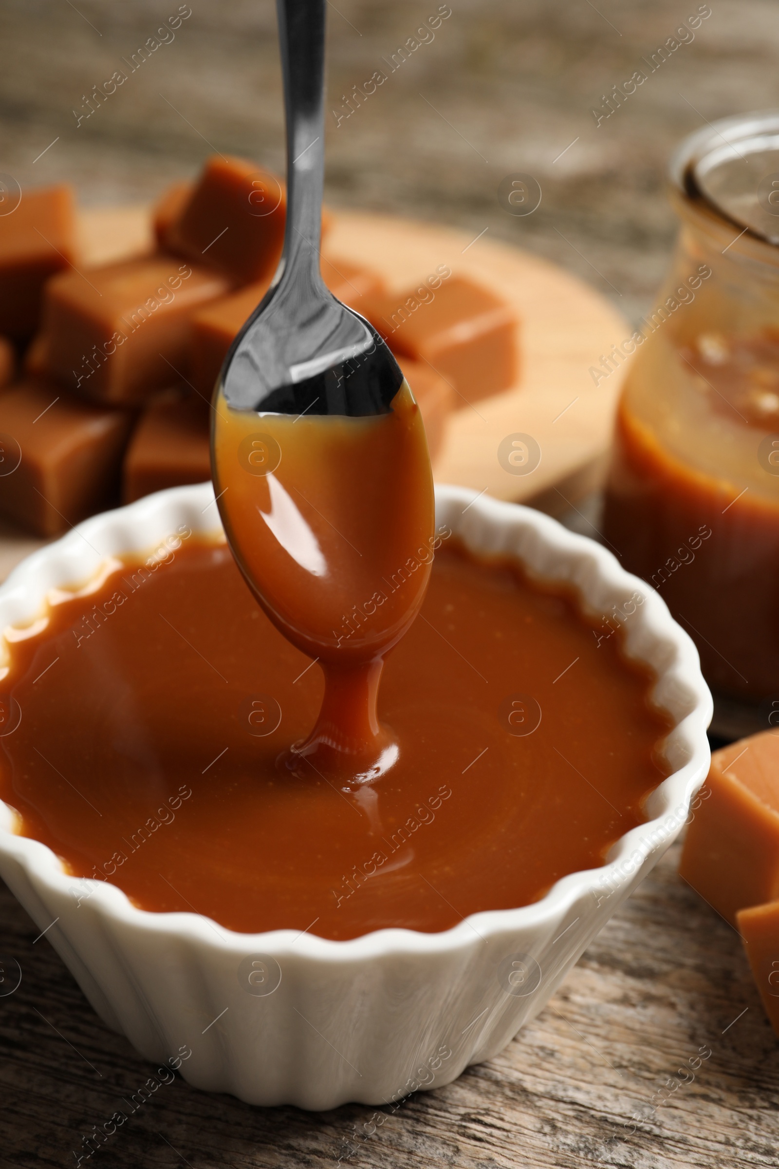 Photo of Taking tasty salted caramel with spoon from bowl at wooden table, closeup