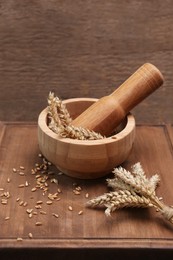 Photo of Mortar with pestle and ears of wheat on wooden table