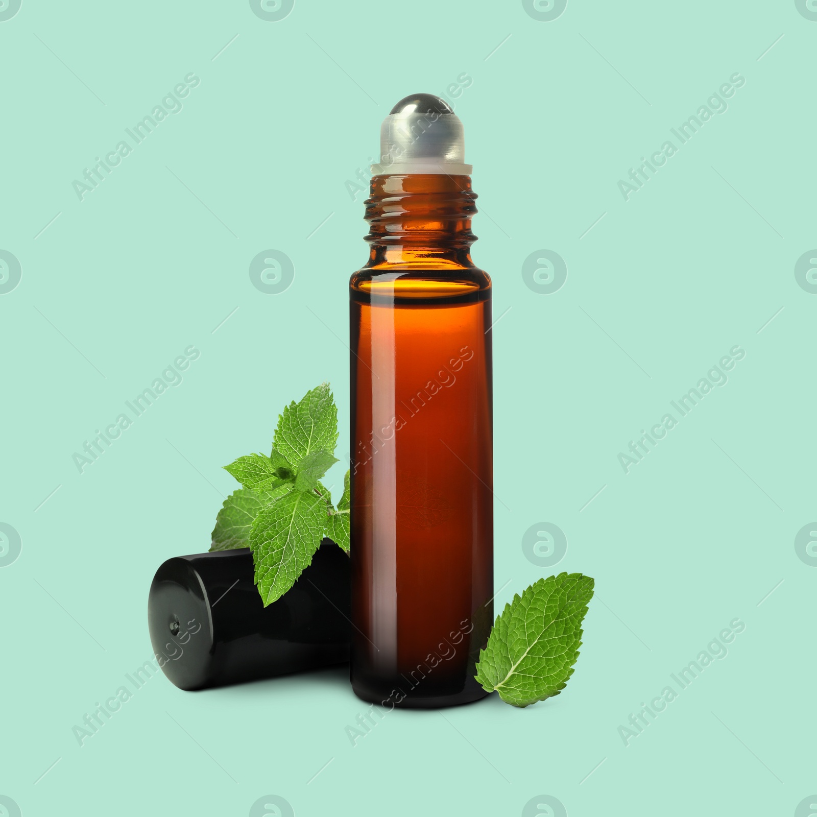 Image of Bottle of mint essential oil and green leaves on pale light blue background