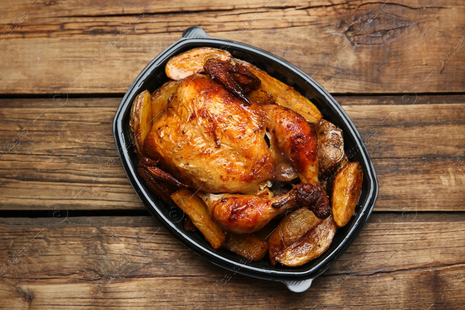 Photo of Delicious grilled chicken with potato in plastic container on wooden table, top view. Food delivery service