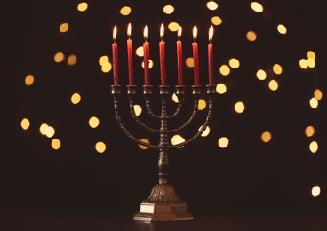 Golden menorah with burning candles against dark background and blurred festive lights