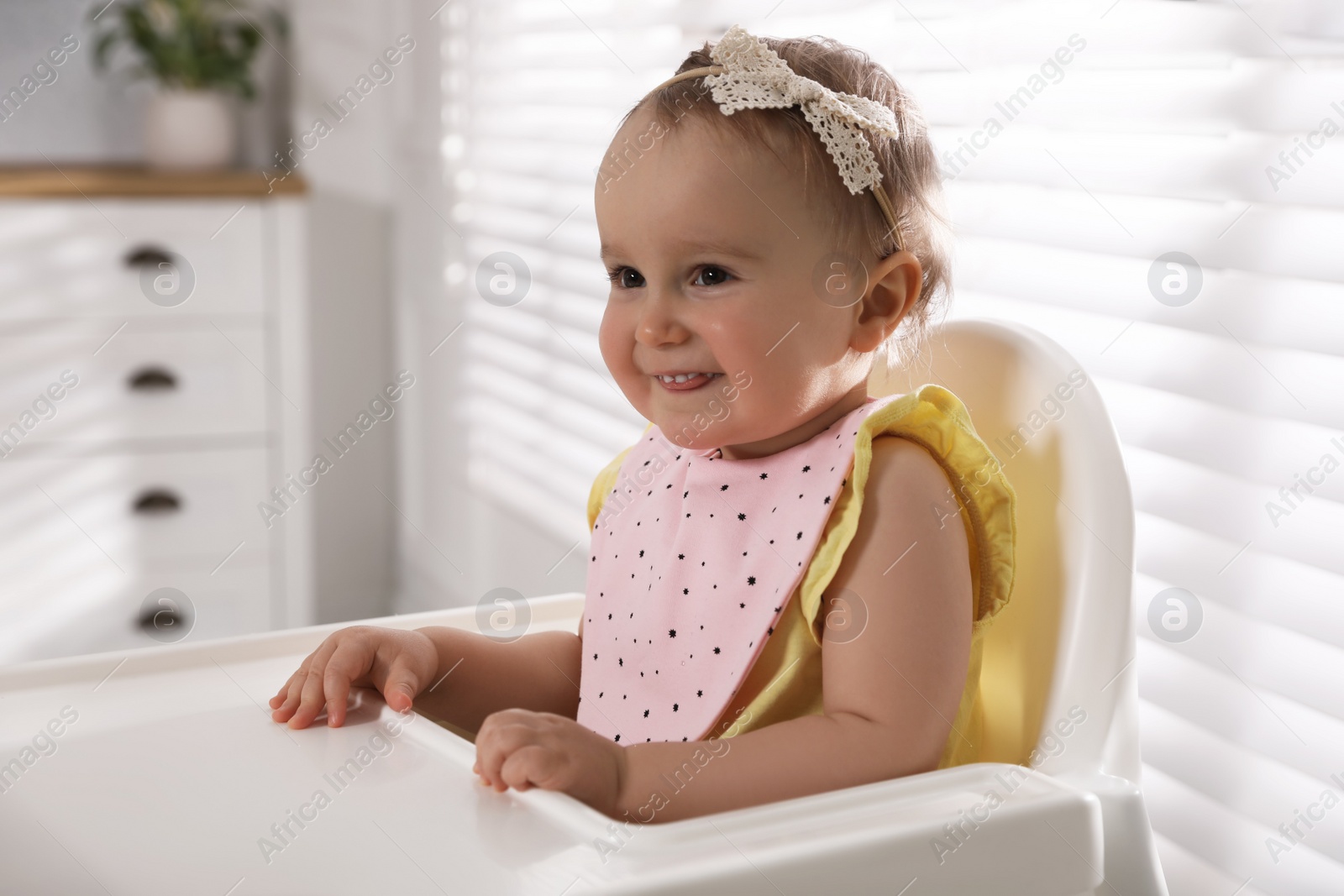 Photo of Cute little baby wearing bib in highchair at home