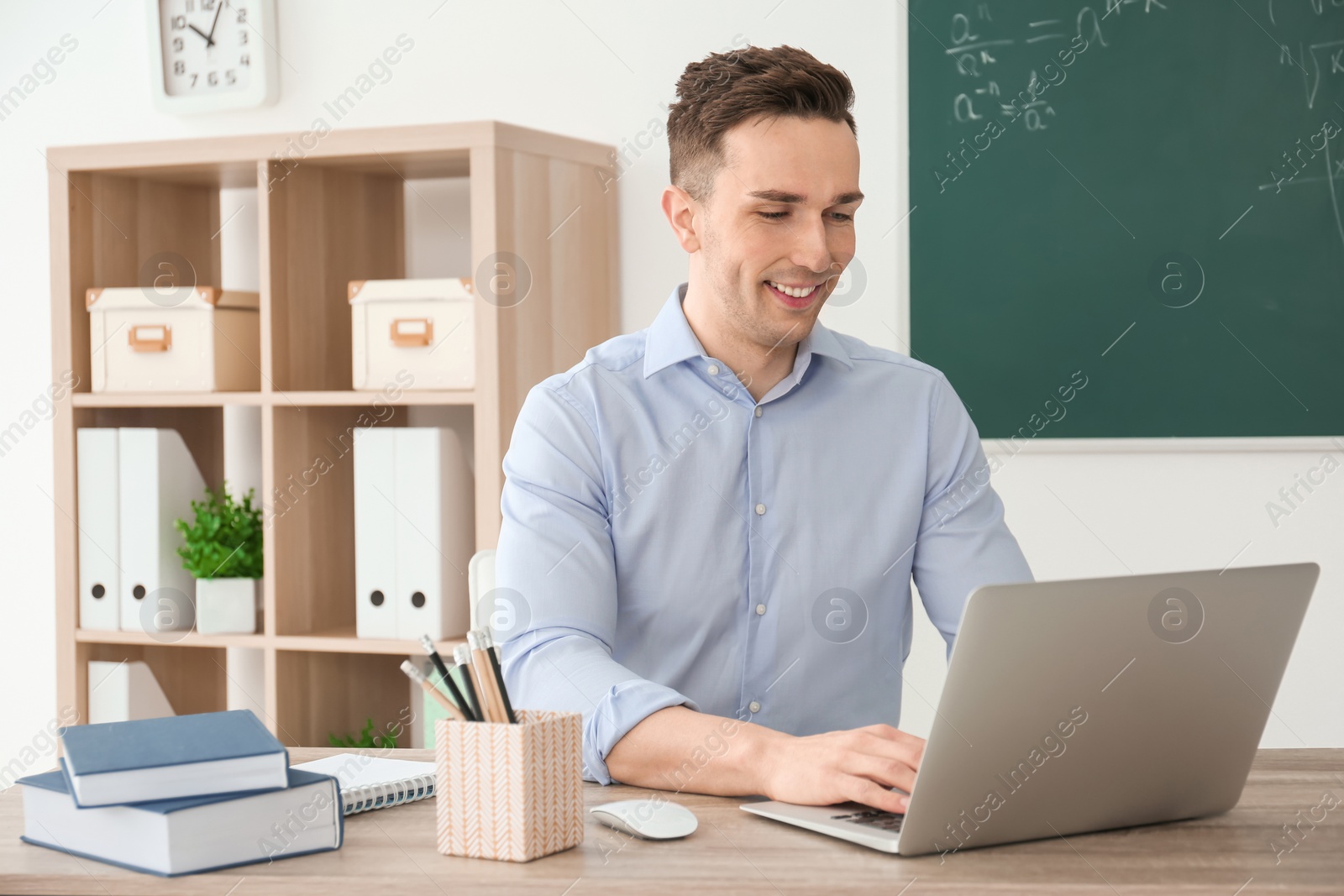 Photo of Young male teacher with laptop sitting at table in classroom