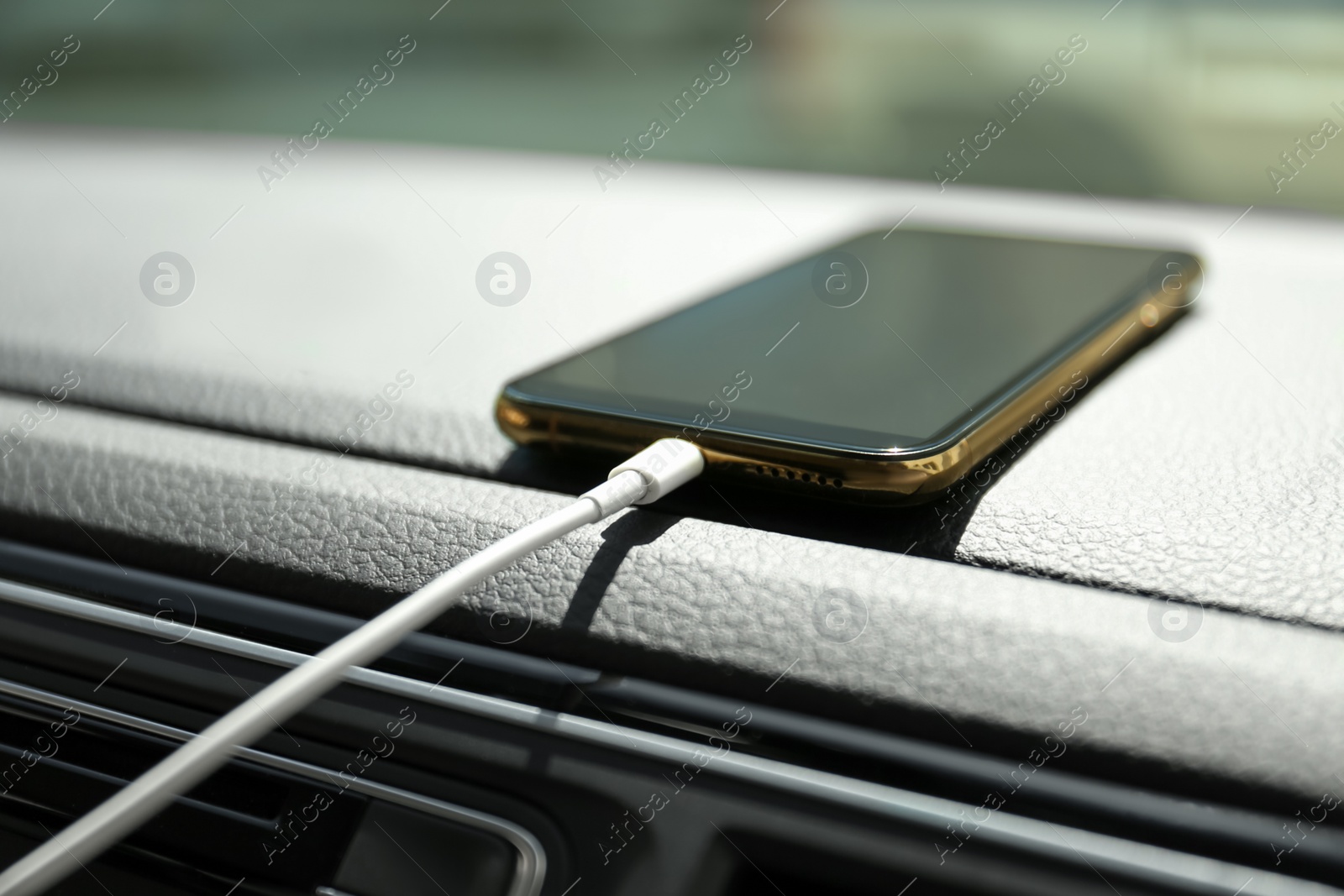 Photo of Smartphone with USB charging cable in modern car, closeup