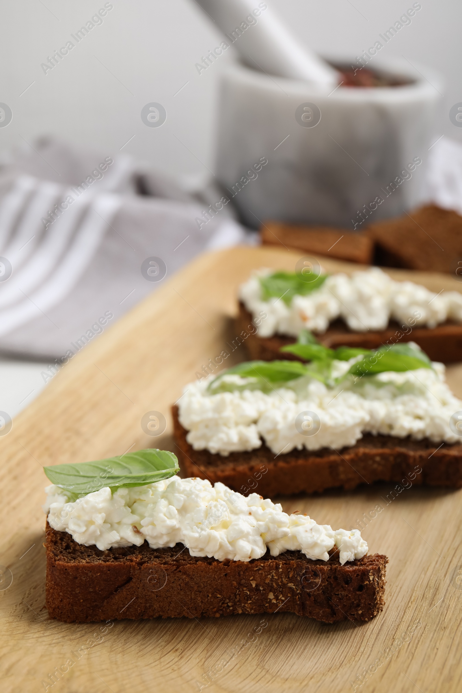 Photo of Bread with cottage cheese and basil on wooden board, closeup