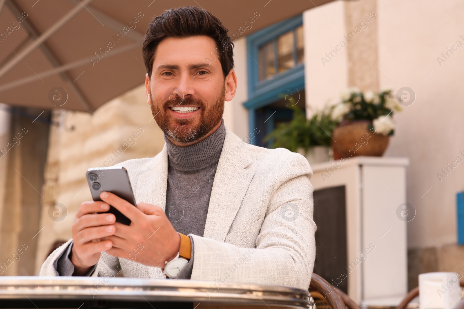 Photo of Handsome man with smartphone at table in outdoor cafe