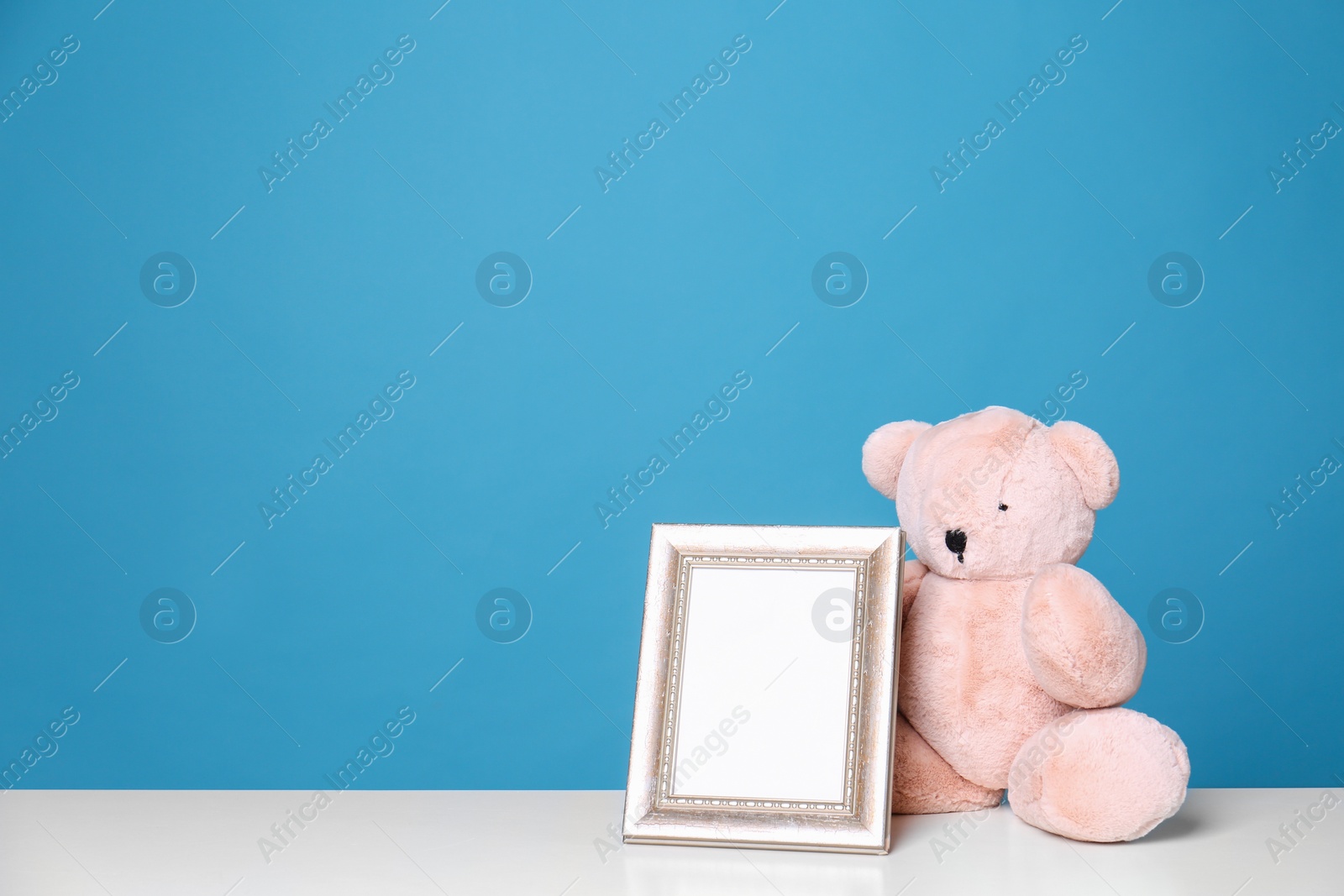 Photo of Photo frame and adorable teddy bear on table against color background, space for text. Child room elements