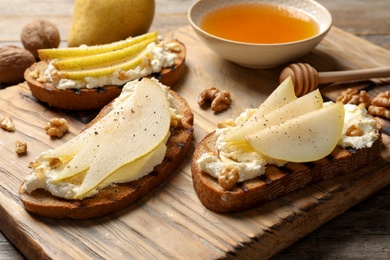 Photo of Toasted bread with tasty cream cheese and pear on wooden board