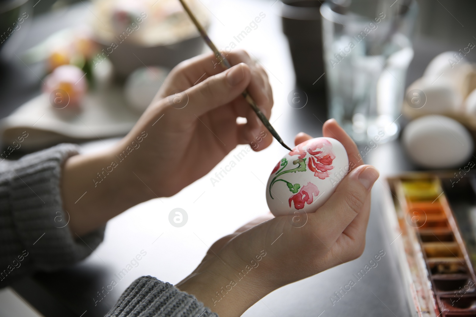 Photo of Woman painting Easter egg at black table, closeup