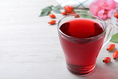 Aromatic rose hip tea and fresh berries on white wooden table, space for text