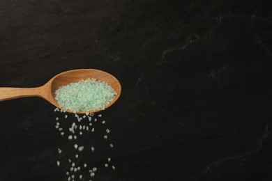 Photo of Pouring turquoise sea salt from wooden spoon against black background. Space for text