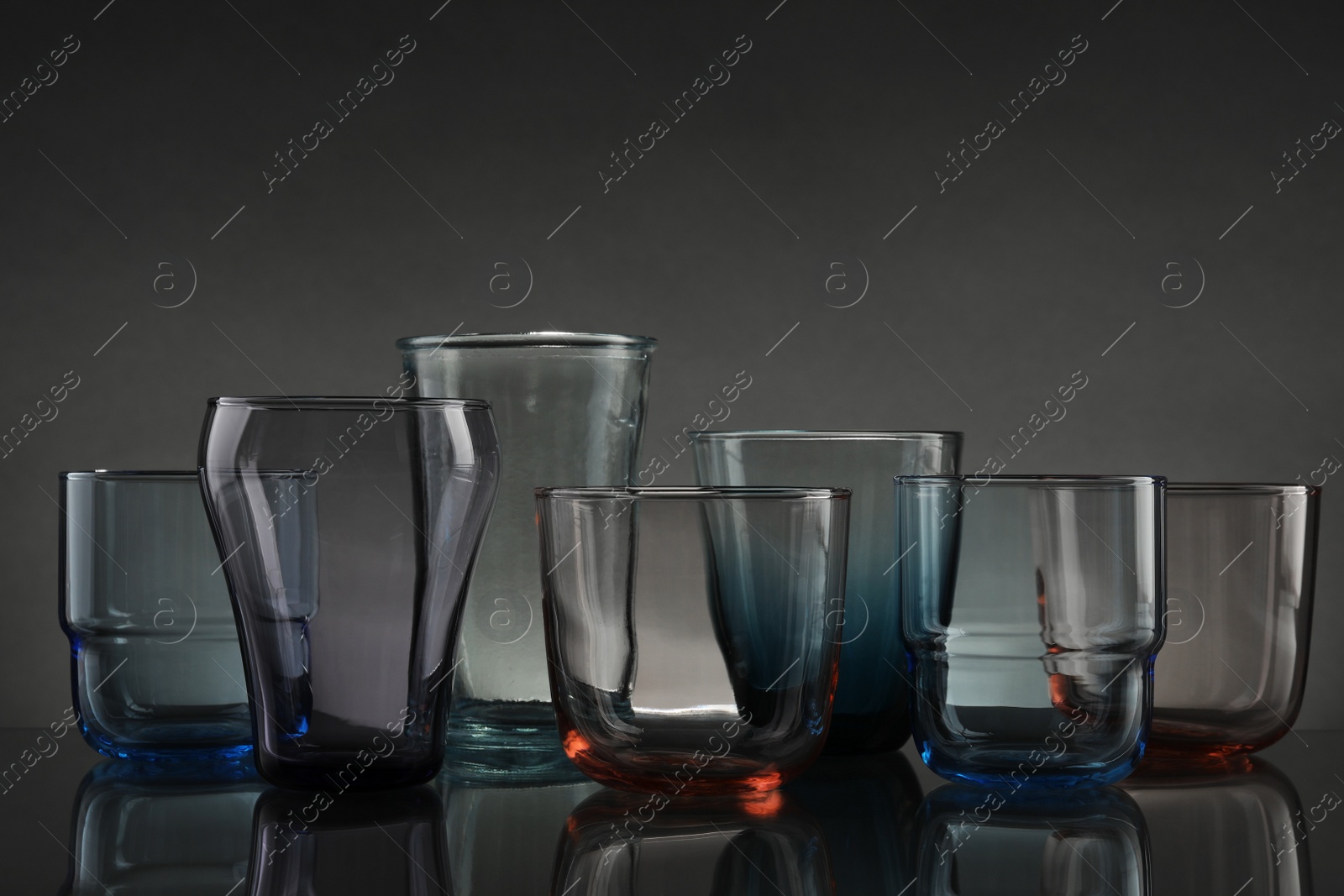 Photo of Set of different colorful empty glasses on table against grey background