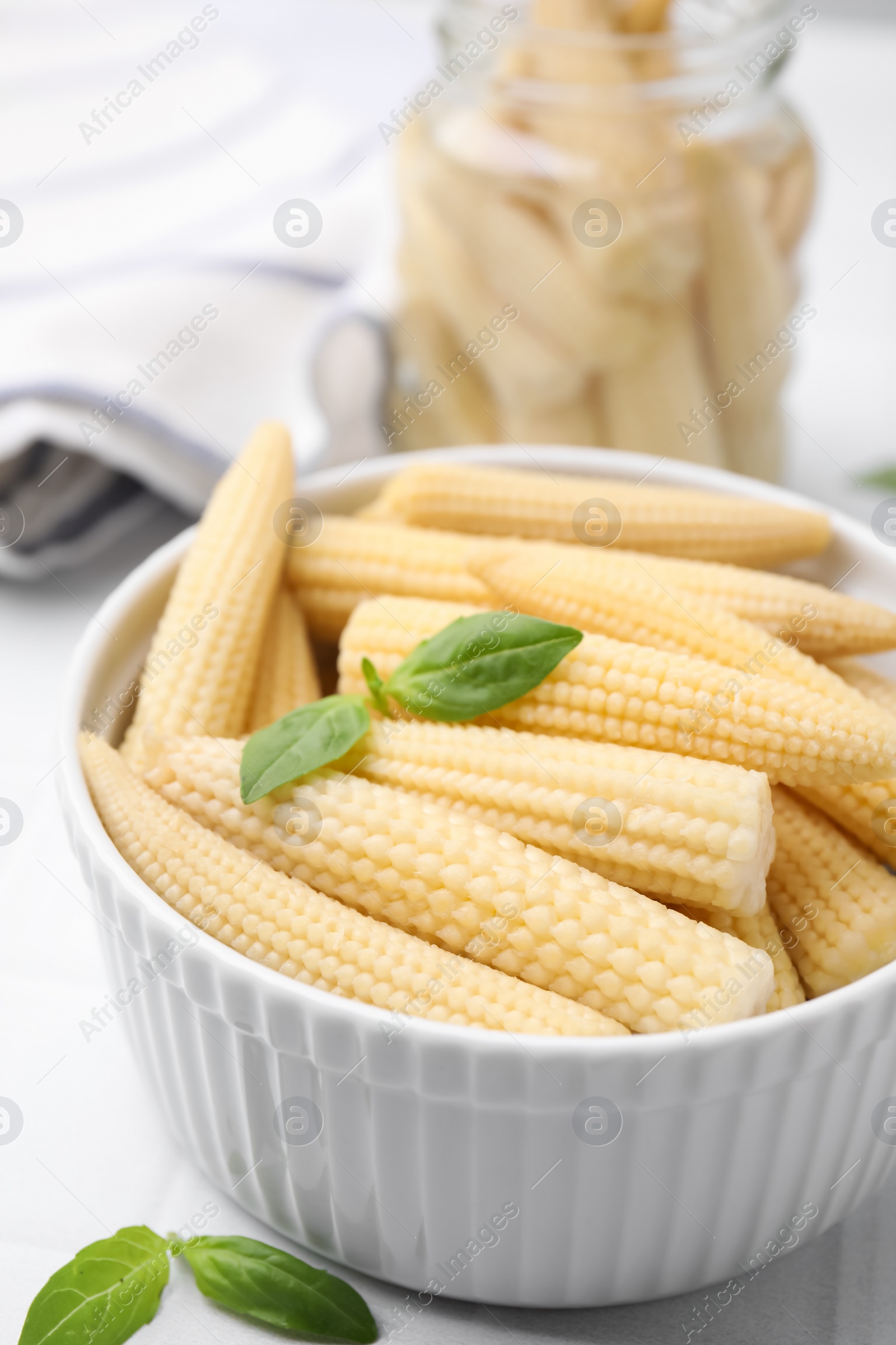 Photo of Canned baby corns with basil on white tiled table, closeup