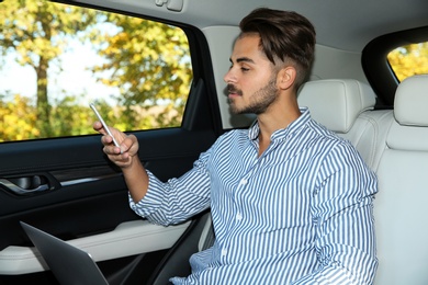 Young handsome man with laptop using phone in car