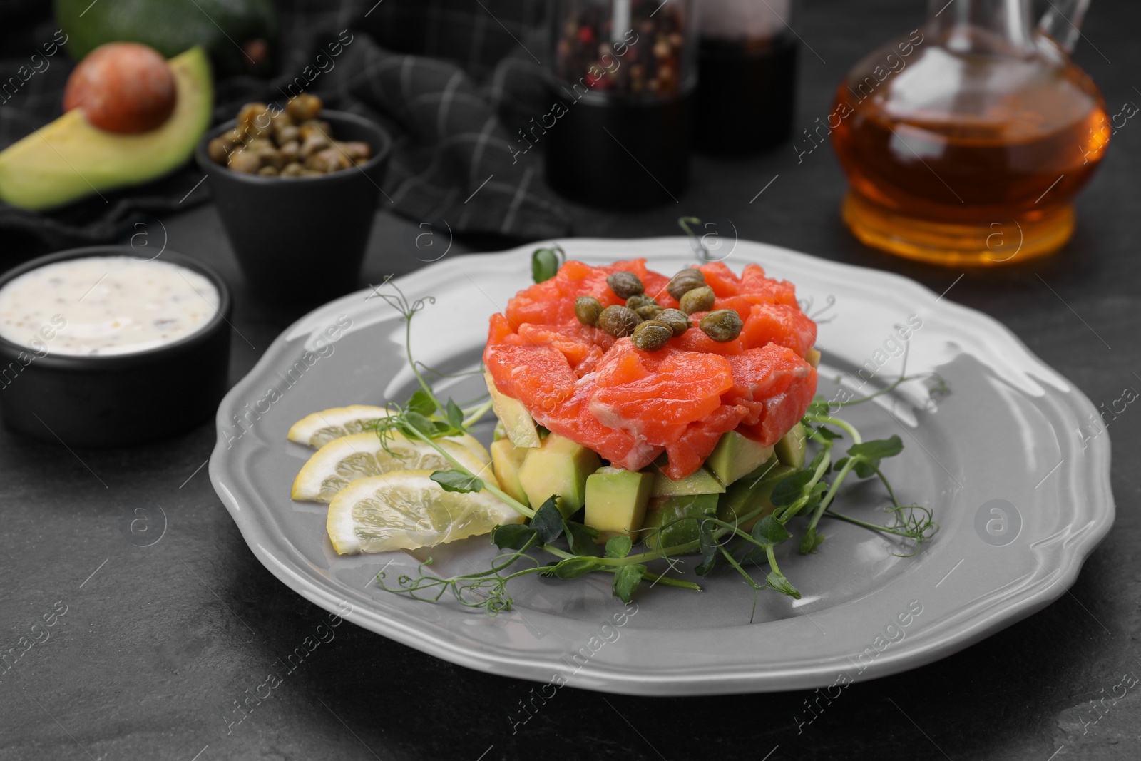 Photo of Delicious salmon tartare served with avocado and lemon on dark table